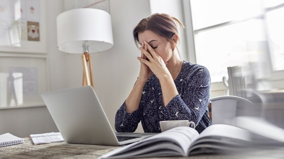 Tired, stressed businesswoman at laptop with head in hands
