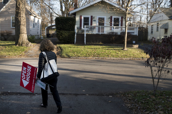 Image: A real estate agent removes an \"Open House\" sign displayed in the front yard of a home for sale in Columbus