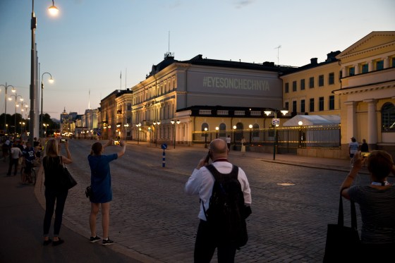 Image: People take pictures of a screen projected sign next to the president's castle in Helsinki