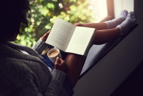 Image: young woman reading a book while enjoying a cup of coffee at home
