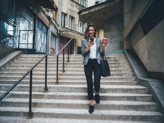 Image: Woman texts and drinks coffee while walking down the stairs