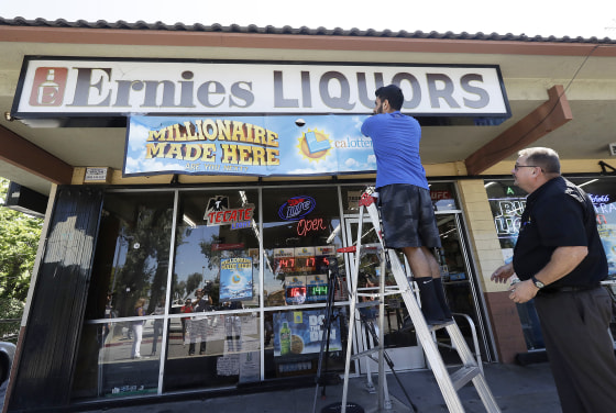Image: California Lottery official Mike Neis, right, watches as Amol Sachdev hangs a sign over his family's store Ernie's Liquors in San Jose, California on July 25, 2018.
