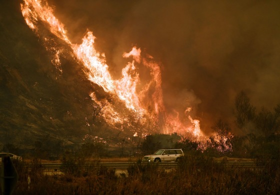 Image: Vehicles pass beside a wall of flames on the 101 highway as it reaches the coast during the Thomas wildfire near Ventura