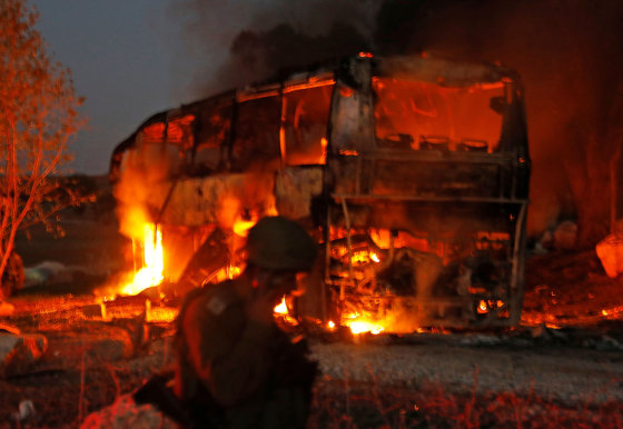 Image: Israeli security forces and firefighters gather near a bus set ablaze after it was hit by a rocket fired from the Palestinian enclave