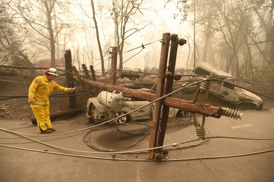 Image: CalFire firefighter Scott Wit surveys burnt out vehicles near a fallen power line on the side of the road after the Camp fire tore through the area in Paradise, California on Nov. 10, 2018.