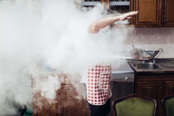 Image: A young man waves smoke away from a burning roast chicken.
