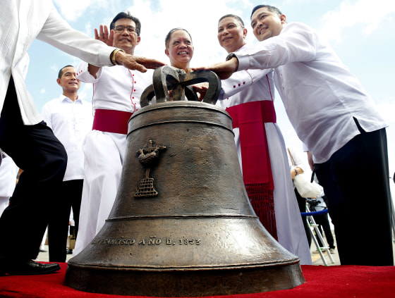 Image: Roman Catholic priest Monsignor Pepe Quitorio, second from left, poses with other priests and officials before one of three church bells seized by American troops as war trophies more than a century ago
