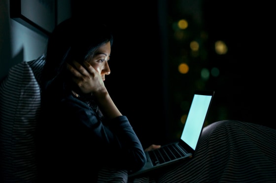 Young woman in deep thought while using laptop on bed at night
