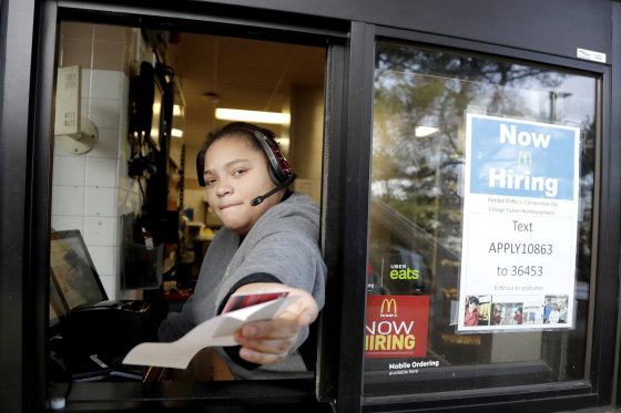 Image: A cashier returns a credit card and a receipt at a McDonald's window, where signage for job openings are displayed,