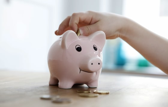 Image: Little boy putting coin into piggy bank, close-up