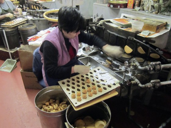 A woman folds and inserts fortunes into cooling cookies at the Golden Gate Fortune Cookie Company, in San Francisco's Chinatown in 2013.
