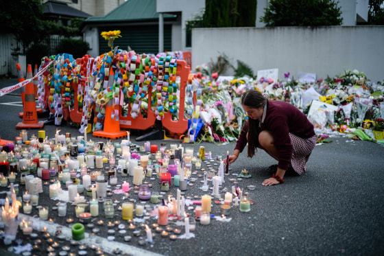 Image: A student places a candle next to flower tributes for the victims after a vigil in Christchurch