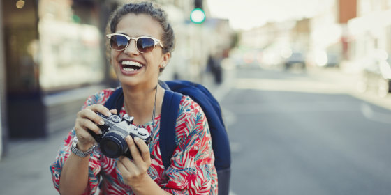 Portrait laughing, enthusiastic young female tourist in sunglasses photographing with camera on urban street