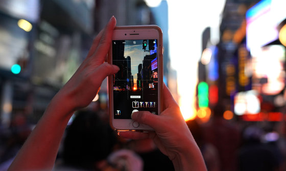 A woman takes a photo with her mobile phone as the sun sets in New York City on July 12, 2018.