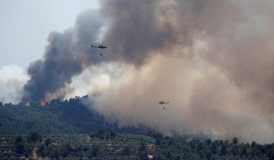 Image: Helicopters drop water over a forest fire during a heatwave near Bovera, west of Tarragona, Spain