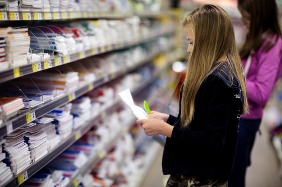 Two girls with shopping list looking for 'back to school' stationery in a store