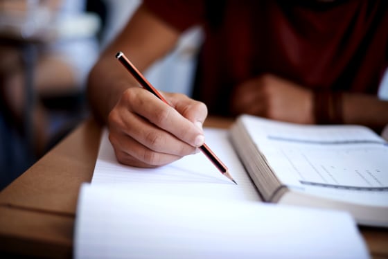 Image: Closeup shot of a young man writing on a note pad