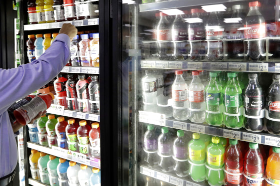 A shop owner reaches into a drink display refrigerator at his convenience store in Kent, Wash on Oct. 1, 2018.