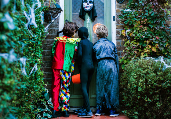 Three boy in halloween costumes, standing at door, trick or treating, rear view