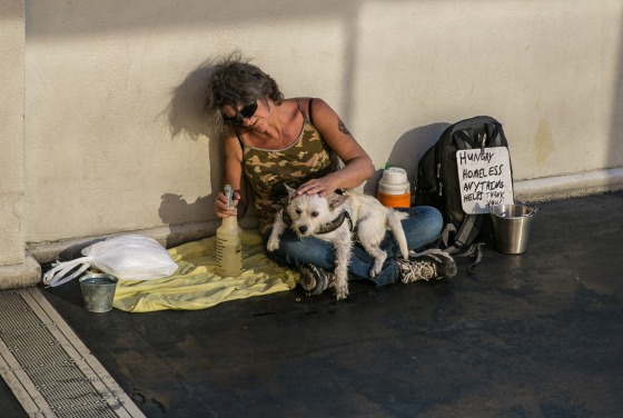 A homeless woman and her dog sit on a pedestrian bridge in the sun as temperatures reached 115 degrees Fahrenheit on July 13, 2017 in Las Vegas.