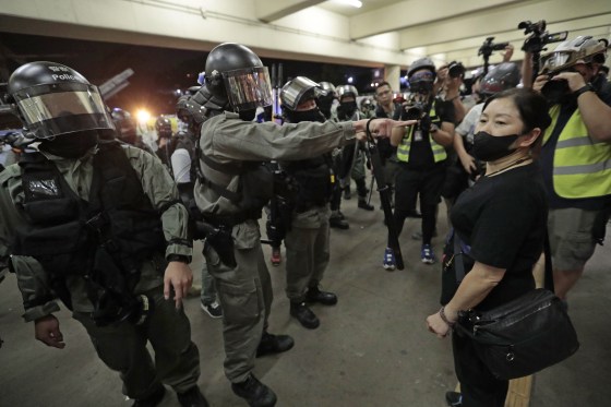 Police in riot gear ask a woman to take off her mask outside a train station in Hong Kong on Sunday. 