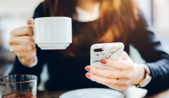 Close up of young woman having coffee and reading news on mobile phone in the early morning before work