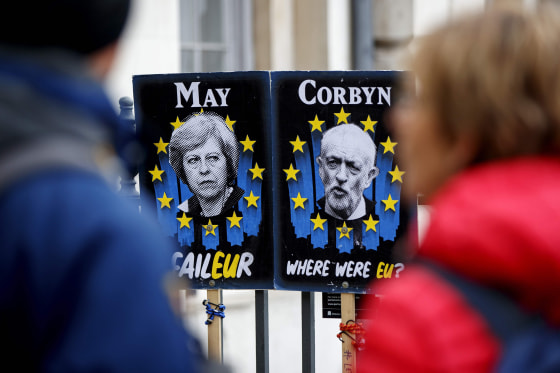 Image: Pedestrians walk past placards featuring Britain's Prime Minister Theresa May and opposition Labour party leader Jeremy Corbyn near the Houses of Parliament