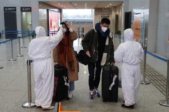 Image: Workers in protective suits check the temperature of passengers arriving at the Xianning North Station in Xianning, a city bordering Wuhan, on Friday.