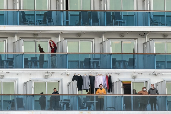 Image: A passenger jogs on the spot as another stretches as they wait on the balconies of their cabins on the Diamond Princess cruise ship as it sits docked at Daikoku Pier