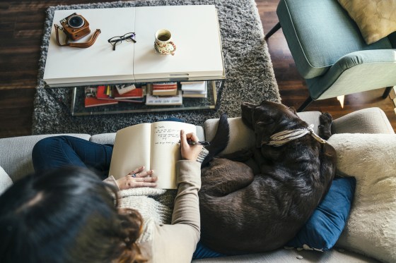 Mixed Race woman on sofa with dog writing in journal