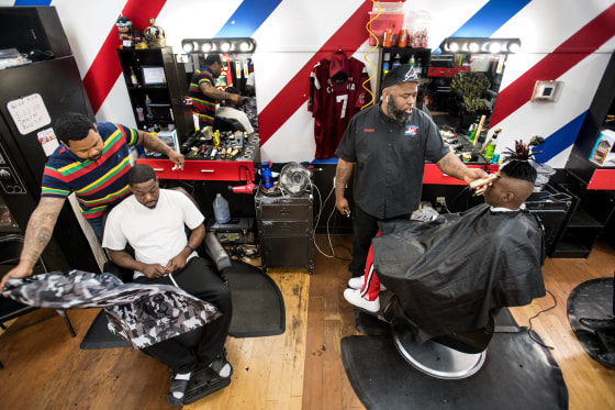 Image: ReCarlo Lewis, owner of Lucciono's barbershop, second right, and Eldred Anderson, left, attend to clients in North Charleston, S.C.