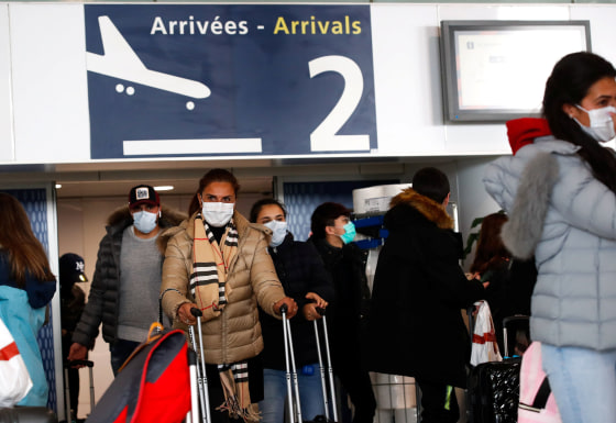 Image: People wearing protective face masks walk at as they arrive at Charles de Gaulle airport in Paris