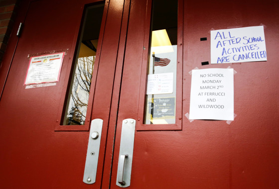 Image: A US flag is reflected in a window as signs announcing a closure and cancelled activities are pictured at Ferrucci Junior High School after two schools were closed for cleaning due to flu-like symptoms of a relative in Puyallup