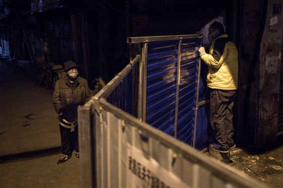 Image: Two men speak over a makeshift barricade to control the entry and exit into a residential area in Wuhan on March 4, 2020.