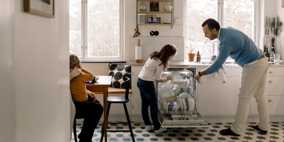 Father and daughter arranging utensils in dishwasher while standing at kitchen