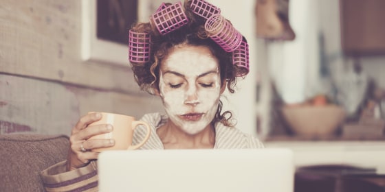 Woman With Hair Curlers Using Laptop On Sofa At Home