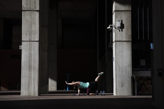 Unable to work out at her gym since it closed due to coronavirus, a woman exercises in a quiet corner at the entrance to City Hall in Boston on March 21, 2020.