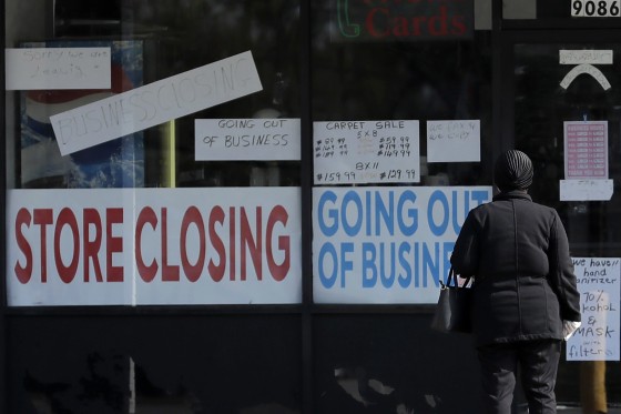 Image: A woman looks at signs at a store closed due to COVID-19 in Niles, Ill.