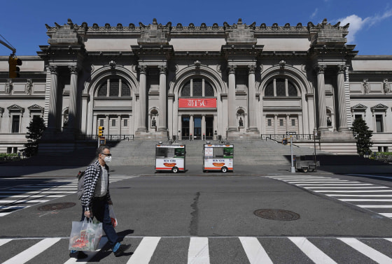 Image: A man wearing a face mask walks past the Metropolitan Museum of Art in New York