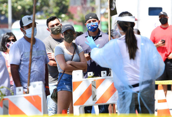 A COVID-19 test site volunteer gives directions to people waiting in line in Los Angeles on July 10, 2020.