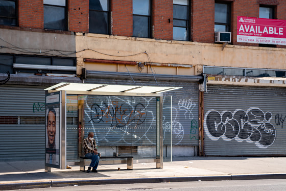 A person sits at a bus stop next to closed businesses in the Brooklyn borough of New York City on June 17, 2020.