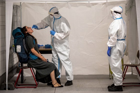 Image: A member of the German Red Cross (DRK) wears a PPE protective suit while taking a throat swab sample from a person at a Covid-19 testing station set up at Hauptbahnhof train station