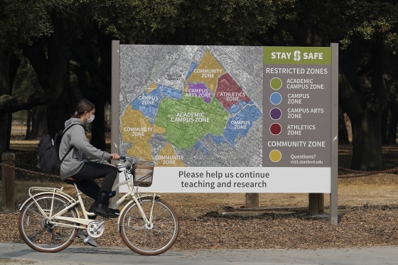Image: A bicyclist rides past a sign showing restricted zones around the Stanford University campus in Stanford, CA.