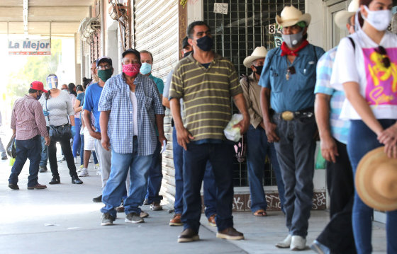 Image: People wear face coverings while waiting in a socially distanced line to enter a bookkeeping shop near the U.S.-Mexico border in Imperial County, which has been hard-hit by the COVID-19 pandemic