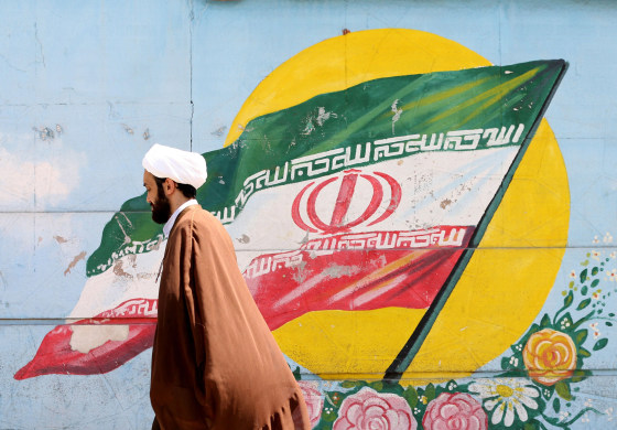 Image: An Iranian cleric walks past a mural painting of the national flag in the capital Tehran.
