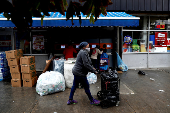 Image: A woman wearing a protective face mask pushes a cart by a recycling center as the spread of coronavirus disease (COVID-19) continues in the borough of Brooklyn in New York