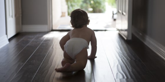 Rear view of baby boy wearing nappy crawling towards open front door