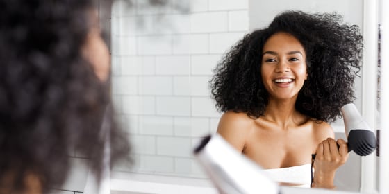 Woman blow drying her hair in a bathroom with a small blow dryer