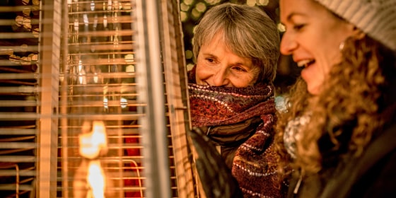 Two woman warming up outside with an electric propane heater