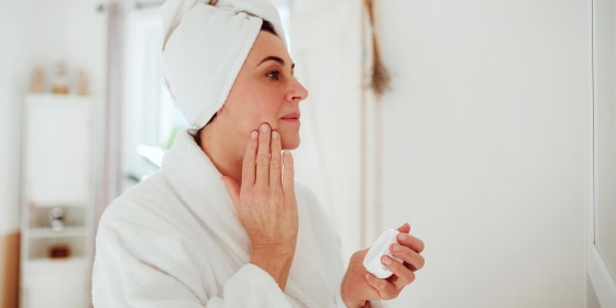 Woman rubbing lotion on her face in a bathrobe, from Dermstore